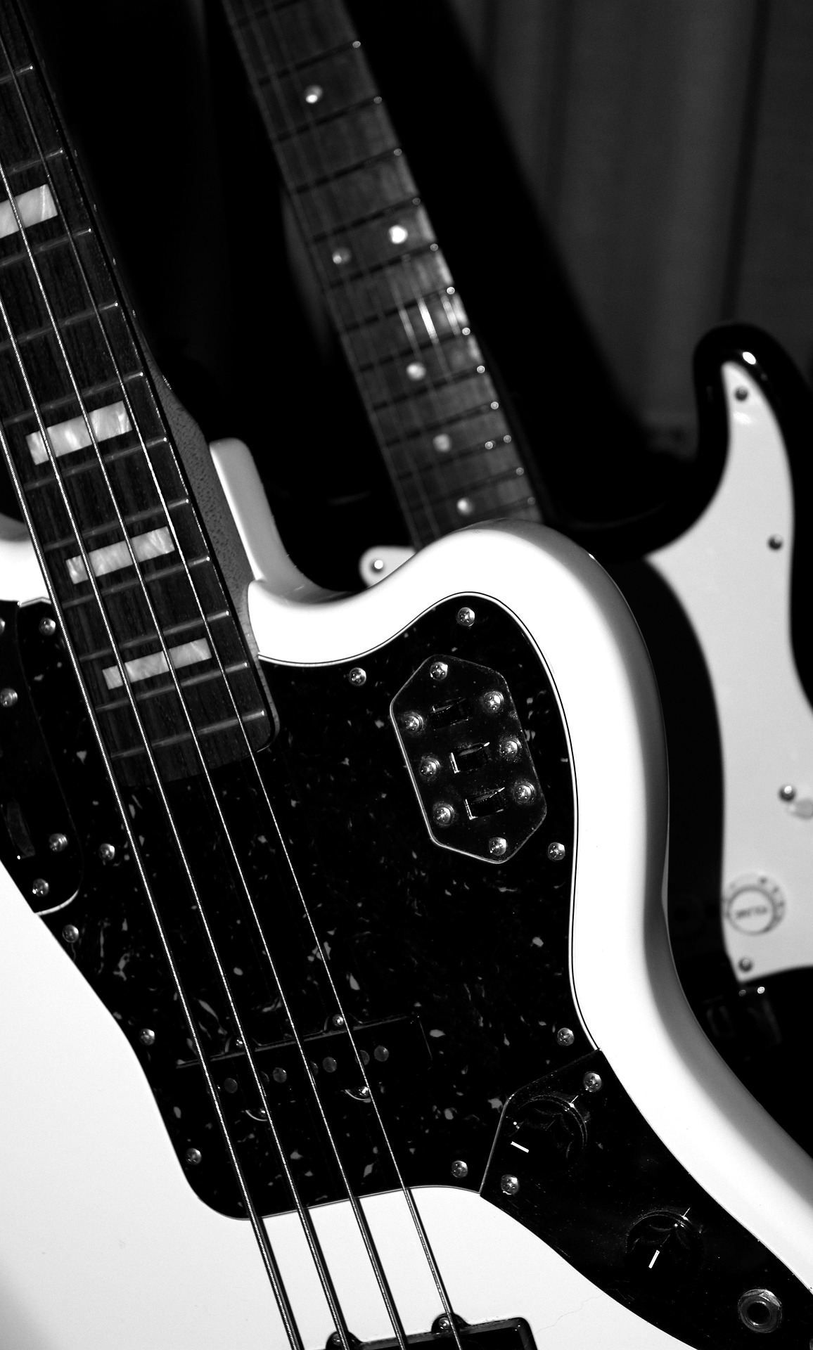 close up van een witte basgitaar die voor een zwarte elektrische gitaar staat